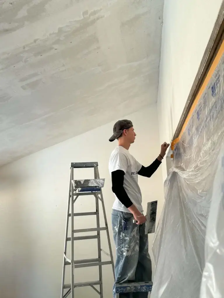 Worker in a Precision Patch shirt taping off a wall before ceiling work